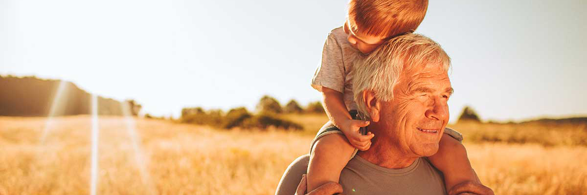 A man carrying a child on his shoulders through a field at sunset